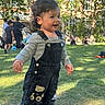 Ethan a rejoint le concours — aidez-le/la à gagner de superbes lots ! background, building, casual_clothing, child, curly_hair, cute, daylight, grass, happy, nature, outdoor, overalls, park, people, play, shoes, smile, sunlight, toddler, trees
