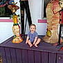 Luca is registered to the contest to win money with this photo: barefoot, casual_clothing, child, cigarette, daylight, decorative_art, happy, metal_sculpture, outdoor, playful, portrait, purple_platform, seated, skeleton, smiling, statue, toddler, umbrella, wall, window