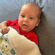 Elijah joined the competition — help win amazing prizes! baby, infant, child, portrait, face, eyes, open_mouth, smiling, red_clothing, blanket, fleece, couch, indoors, close_up, sitting, lying_down, looking_at_camera, soft_texture, patterned_blanket, family_photo