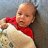 baby, infant, child, portrait, face, eyes, open_mouth, smiling, red_clothing, blanket, fleece, couch, indoors, close_up, sitting, lying_down, looking_at_camera, soft_texture, patterned_blanket, family_photo