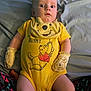 baby, infant, yellow_onesie, mittens, winnie_the_pooh, bed, blanket, patterned_pants, curious_expression, lying_down, child, person, cute, indoors, soft_lighting, clothing, portrait, small_child, sleepwear, yellow
