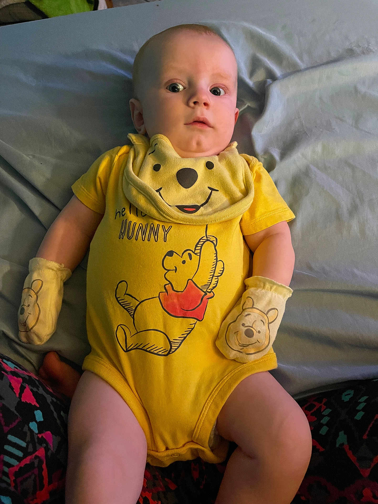 Jaxson is registered to the contest to win money with this photo: baby, infant, yellow_onesie, mittens, winnie_the_pooh, bed, blanket, patterned_pants, curious_expression, lying_down, child, person, cute, indoors, soft_lighting, clothing, portrait, small_child, sleepwear, yellow