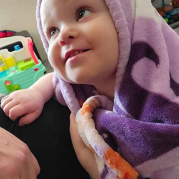 Mckensey is registered to the contest to win money with this photo: baby, blanket, child, closeup, cozy, cute, expression, face, happy, indoor, infant, person, playroom, purple, smiling, soft, toddler, toy, wrapped, young