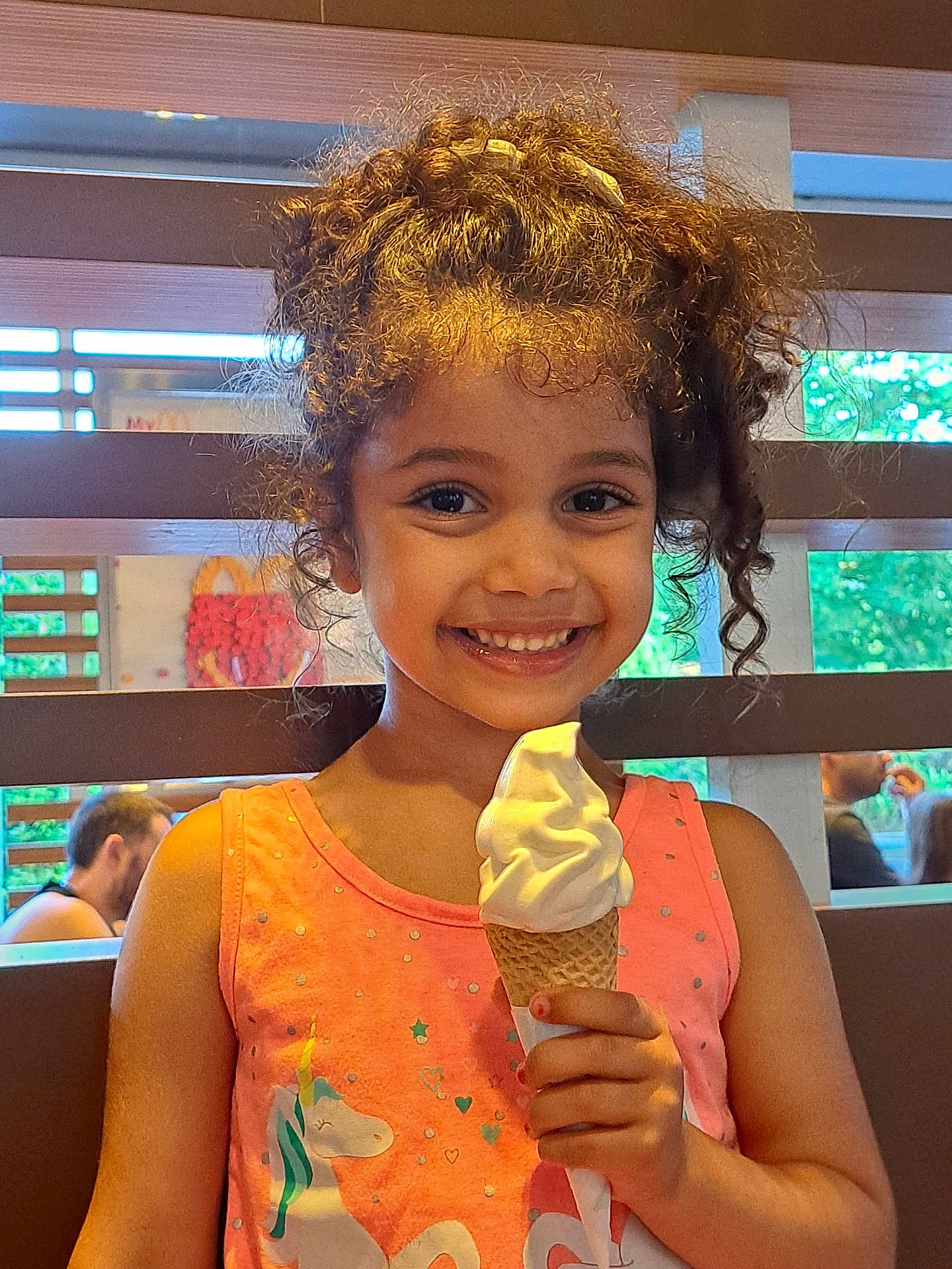 Eimy participe au concours pour gagner de l'argent avec cette photo : child, girl, ice_cream, soft_serve, cone, smile, curly_hair, pink_dress, unicorn, indoor, happy, person, food, dessert, summer, cute, portrait, sitting, background, people