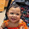 baby, child, smiling, orange_clothing, stroller, butterfly_pattern, happy, cute, earrings, portrait, indoor, infant, toddler, face, human, seat, bright_colors, cheerful, baby_girl, closeup