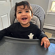 Daryl is registered to the contest to win money with this photo: baby, black_shirt, child, cozy, cute, door, face, furniture, ghost_emblem, hands, happy, high_chair, home, indoor, person, portrait, smiling, toddler, window, young_child