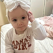 Nevaeh joined the competition — help win amazing prizes! toddler, child, baby, headband, white_clothing, shirt, text_on_clothing, bed, indoor, portrait, cute, baby_girl, hand, face, expression, furniture, blanket, soft_lighting, room, person