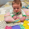 baby, infant, pillow, bed, blanket, pop_it_toys, colorful, curious, surprised, clothing, patterned, indoor, cute, child, person, toy, playful, expression, young, face