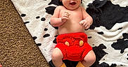 Jordan Jr is registered to the contest to win money with this photo: baby, infant, smiling, hat, crocheted_clothing, red_shorts, yellow_booties, black_and_white_blanket, carpet, person, legs, socks, tattoo, hand, happy, lying_down, indoor, cozy, cute, playful
