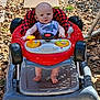 baby, baby_walker, outdoor, sunlight, rocks, stepping_stones, bib, red, gray, toys, foot, face, child, clothing, person, seat, play, summer, cute, expression