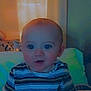 Jay is registered to the contest to win money with this photo: baby, child, indoor, striped_shirt, bed, pillow, blanket, face, portrait, sitting, curtains, soft_lighting, cozy, infant, young_child, expression, cute, person, home, relaxed