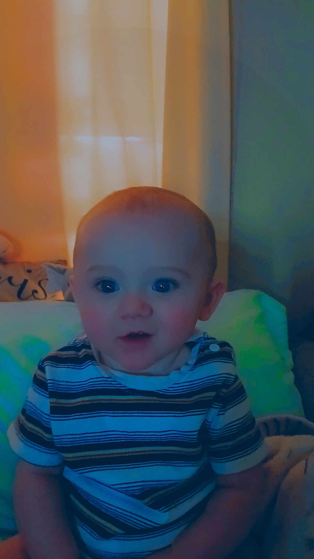 Jay is registered to the contest to win money with this photo: baby, child, indoor, striped_shirt, bed, pillow, blanket, face, portrait, sitting, curtains, soft_lighting, cozy, infant, young_child, expression, cute, person, home, relaxed