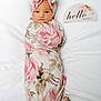 Everleigh is registered to the contest to win money with this photo: baby, newborn, infant, swaddled, floral_pattern, blanket, headwrap, pink, white_background, face, portrait, cute, resting, child, soft_lighting, decor, sign, hello_world, wrapped, peaceful