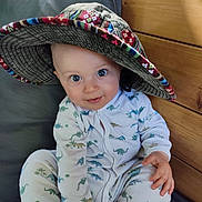 Aurèle participe au concours pour gagner de l'argent avec cette photo : baby, child, hat, pajamas, dinosaur_pattern, smile, blue_eyes, wooden_wall, cushion, seated, indoors, cute, infant, face, hand, clothing, portrait, happy, cozy, playful
