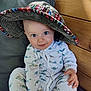 baby, child, hat, pajamas, dinosaur_pattern, smile, blue_eyes, wooden_wall, cushion, seated, indoors, cute, infant, face, hand, clothing, portrait, happy, cozy, playful
