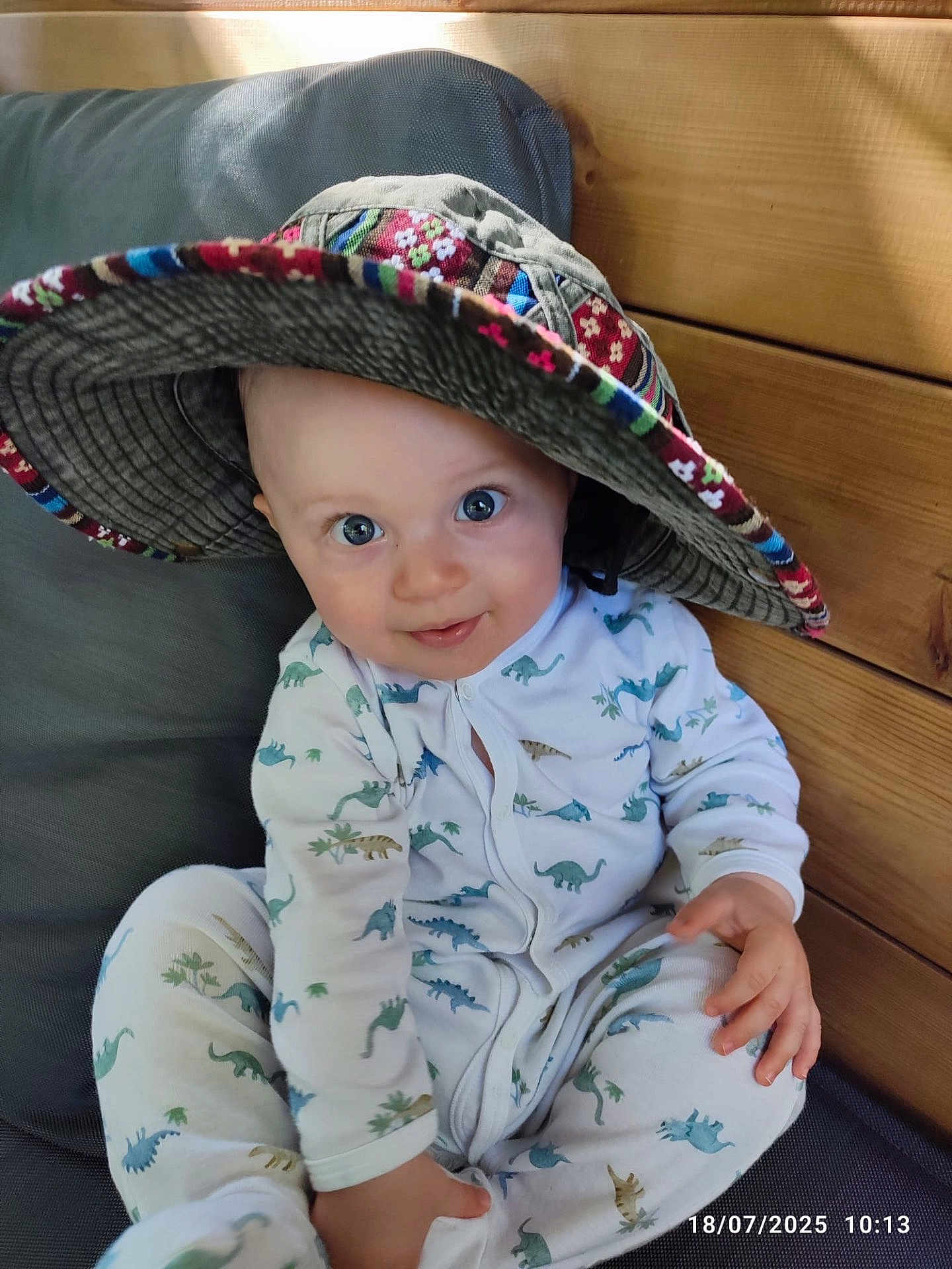 Aurèle participe au concours pour gagner de l'argent avec cette photo : baby, child, hat, pajamas, dinosaur_pattern, smile, blue_eyes, wooden_wall, cushion, seated, indoors, cute, infant, face, hand, clothing, portrait, happy, cozy, playful