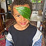 child, leaf, eye_patch, indoor, curly_hair, smile, black_shirt, jacket, fruit, carpet, scooter, window, table, chair, home, playful, person, portrait, happy, casual