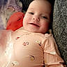 baby, infant, child, smiling, happy, portrait, close_up, indoor, couch, blanket, cushion, pink_clothing, onesie, heart_pattern, floral_pattern, lying_down, face, eyes, cozy, photography