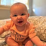 baby, child, infant, smiling, happy, sitting, portrait, indoors, blanket, floral_blanket, orange_clothing, romper, short_sleeves, bald, blue_eyes, open_mouth, window, soft_lighting, cozy, close_up
