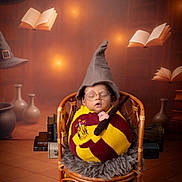 Krishiv is registered to the contest to win money with this photo: baby, infant, sleeping, wizard_hat, glasses, wand, gryffindor_scarf, costume, rattan_chair, faux_fur, studio_backdrop, floating_books, books, potions, magical, cozy, portrait, props, warm_lighting, novice_wizard