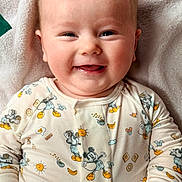 Remi joined the competition — help win amazing prizes! baby, infant, smiling, onesie, mickey_mouse, blanket, close_up, face, cheeks, tongue, happy, adorable, lying_down, pajamas, drool, eyes, hair, skin, portrait, cute