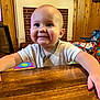 baby, child, smiling, wooden_table, indoor, toy, colorful, face, person, happy, blond_hair, short_sleeve_shirt, playroom, fireplace, brick, wood_paneling, furniture, candid, cute, infant