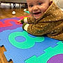 baby, child, smiling, happy, hooded_sweater, puzzle_mat, colorful, floor, indoor, person, cute, toddler, playtime, blue_eyes, wooden_floor, cozy, clothing, face, expression, home