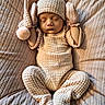 newborn, baby, sleeping, portrait, knitted_clothing, winter_hat, mittens, pom_pom, blanket, bedding, cozy, peaceful, infant, closed_eyes, indoor, soft_lighting, textile, brown_tones, lying_down, cute