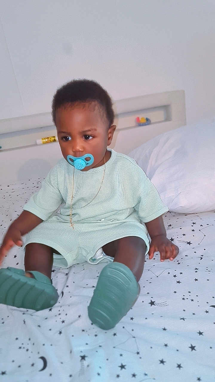 Mahel a rejoint le concours — aidez-le/la à gagner de superbes lots ! toddler, child, pacifier, bed, bedspread, star_pattern, mint_green_clothing, shoes, necklace, indoor, cute, sitting, young_child, person, portrait, baby, furniture, decor, sleeping_area, casual