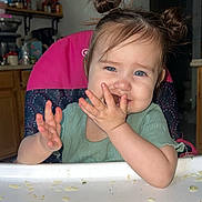 Azarliah Esme is registered to the contest to win money with this photo: toddler, child, high_chair, food, messy, kitchen, hair_buns, smiling, blue_eyes, green_shirt, hands, face, snack, table, indoor, baby, cute, person, plate, eating