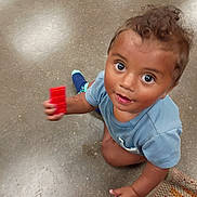 Knowledge is registered to the contest to win money with this photo: toddler, child, toy, block, floor, curly_hair, blue_shirt, indoor, play, looking_up, bright_eyes, skin, hand, kneeling, rug, colorful, casual_clothing, young_child, expression, innocence