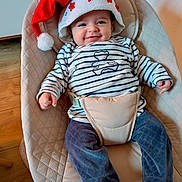 Lucas participe au concours pour gagner de l'argent avec cette photo : baby, santa_hat, striped_shirt, baby_seat, cushion, smile, indoor, wood_floor, pants, clothing, person, happy, festive, infant, cute, headwear, seatbelt, comfort, portrait, holiday