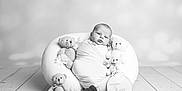 Maeve is registered to the contest to win money with this photo: baby, infant, swaddled, teddy_bear, plush, pillow, flower, wooden_floor, black_and_white, portrait, cute, two_months, wrapped, soft_texture, flooring, child, newborn, decor, sitting, studio