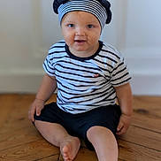 Ayden participe au concours pour gagner de l'argent avec cette photo : toddler, child, striped_shirt, beret, hat, red_pom_pom, blue_eyes, sitting, wooden_floor, barefoot, indoor, curious, smiling, person, flooring, casual_clothing, young_child, portrait, headwear, cute