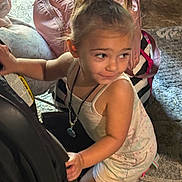 Ariyah is registered to the contest to win money with this photo: toddler, child, car_seat, backpack, indoor, carpet, curly_hair, ponytail, necklace, clothing, playful, person, young_child, floor, bag, smiling, candid, light, portrait, cute