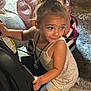 toddler, child, car_seat, backpack, indoor, carpet, curly_hair, ponytail, necklace, clothing, playful, person, young_child, floor, bag, smiling, candid, light, portrait, cute