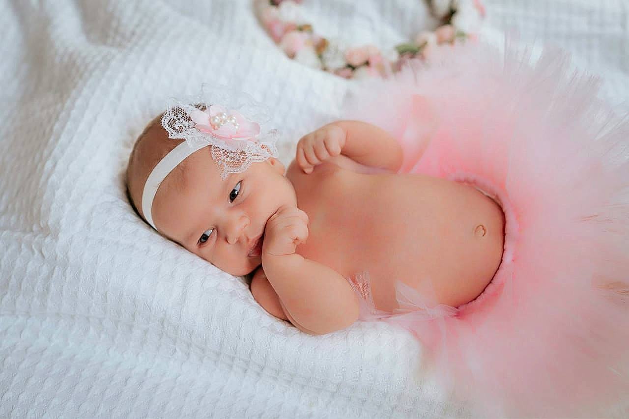 Thalia participe au concours pour gagner de l'argent avec cette photo : arm, baby, baby_sleeping, baby_toddler_clothing, child, comfort, dress, eye, fashion_accessory, headband, headgear, headpiece, headwear, human_body, linens, lip, pattern, peach, person, pink