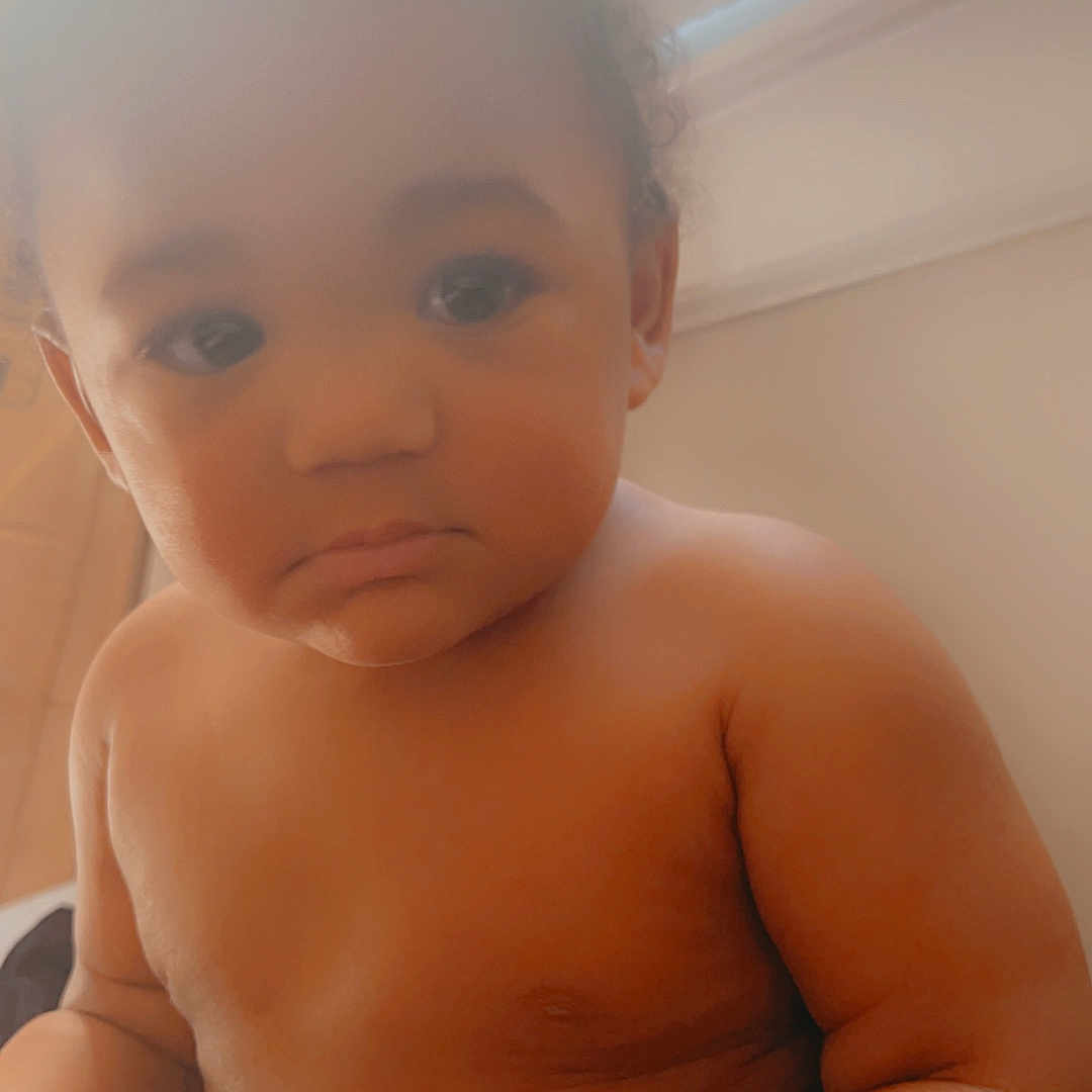 Zorian is registered to the contest to win money with this photo: baby, blinds, child, closeup, curly_hair, face, hands, human, indoor, infant, natural_light, portrait, room, serious_expression, sitting, skin, soft_light, warm_tone, window, young_child