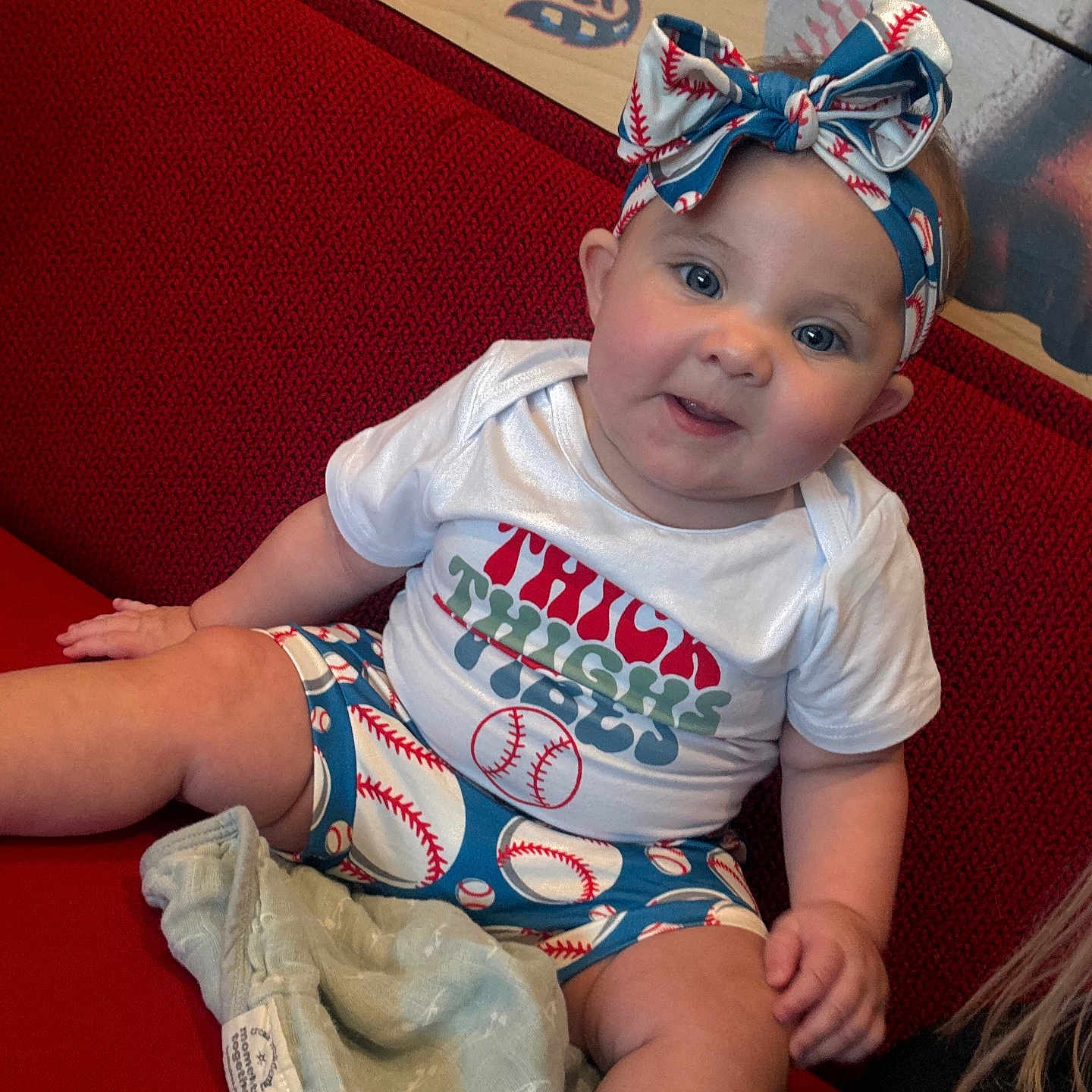 Emori is registered to the contest to win money with this photo: baby, baseball, blanket, child, clothing, couch, cute, face, happy, headband, homedecor, indoor, person, plush, portrait, red, shorts, sitting, smiling, soft