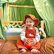 Harold a rejoint le concours — aidez-le/la à gagner de superbes lots ! toddler, child, pumpkin, orange_overalls, hat, barefoot, brown_blanket, wooden_crib, green_fabric, tent, smiling, happy, indoors, cute, baby, playful, fall_theme, cozy, person, portrait