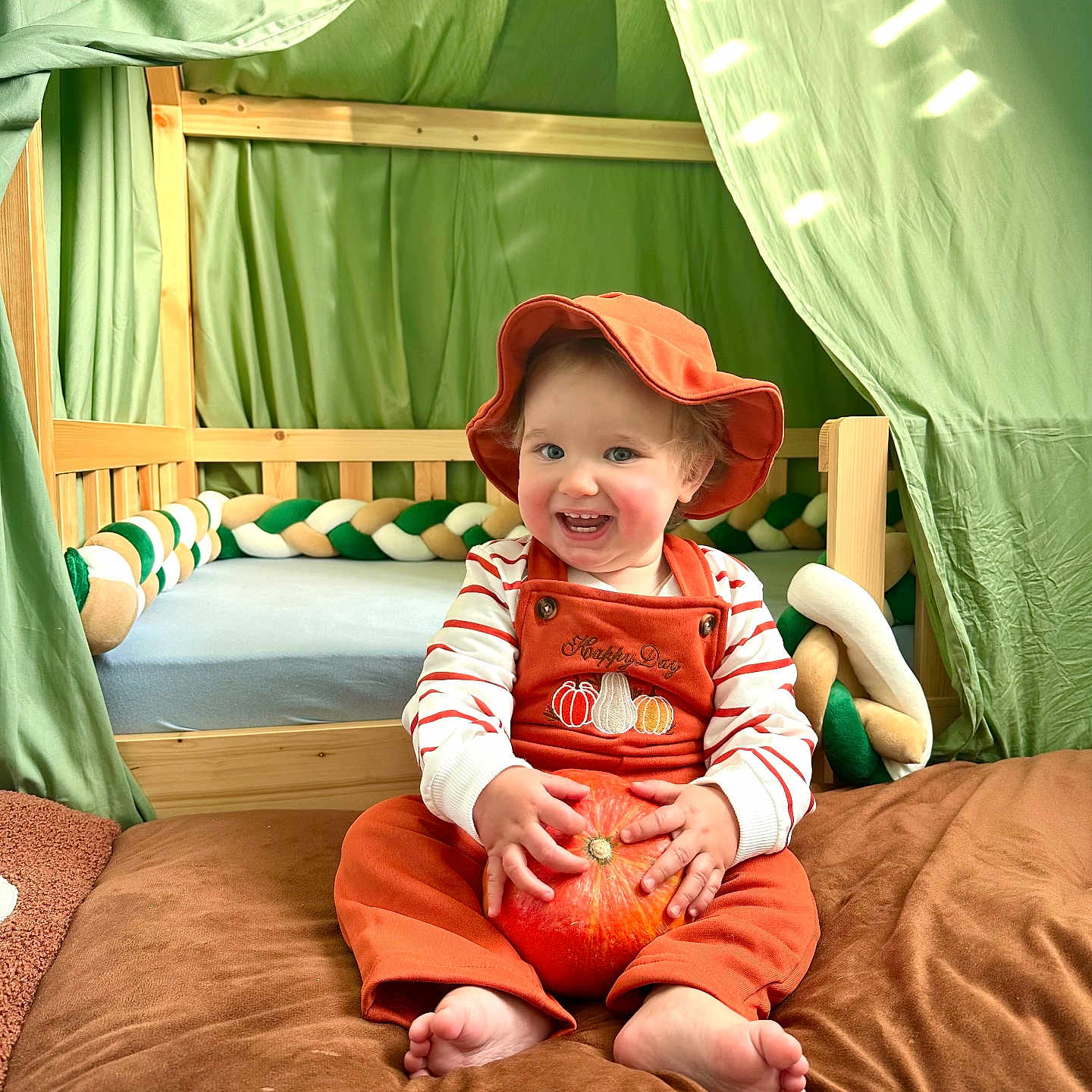 Harold a rejoint le concours — aidez-le/la à gagner de superbes lots ! toddler, child, pumpkin, orange_overalls, hat, barefoot, brown_blanket, wooden_crib, green_fabric, tent, smiling, happy, indoors, cute, baby, playful, fall_theme, cozy, person, portrait