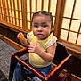 Marisol is registered to the contest to win money with this photo: toddler, child, high_chair, food, yellow_shirt, jeans, pigtails, indoor, wooden_furniture, face, person, seated, curious_expression, restaurant, table, carpet, cute, young_child, eating, casual_clothing