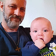 Mateo is registered to the contest to win money with this photo: adult, baby, beard, casual, child, clothing, cross_necklace, curious, cute, face, hand, holding, indoor, man, plush_toy, portrait, sitting, smile, sweater, wall