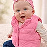 baby, blue_eyes, casual_wear, child, clothing, cozy, cute, hands, happy, headband, headwear, indoor, infant, pink_vest, portrait, puffy_jacket, sitting, smiling, soft_background, warm_clothes
