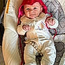 baby, infant, red_hat, devil_horns, onesie, hedgehog_embroidery, smile, face, baby_seat, cushion, cozy, cute, child, lying_down, indoor, soft_lighting, clothing, pacifier_clip, happy, portrait