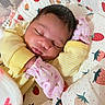 newborn, baby, sleeping, infant, face, portrait, yellow_clothing, pink_clothing, blanket, strawberry_pattern, bed, cozy, peaceful, indoors, close_up, dark_hair, closed_eyes, swaddled, nursery, cute