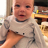 Joshua is registered to the contest to win money with this photo: baby, infant, child, striped_clothing, onesie, hand, face, smile, indoor, living_room, furniture, television, curtains, person, cute, happy, portrait, closeup, skin, head