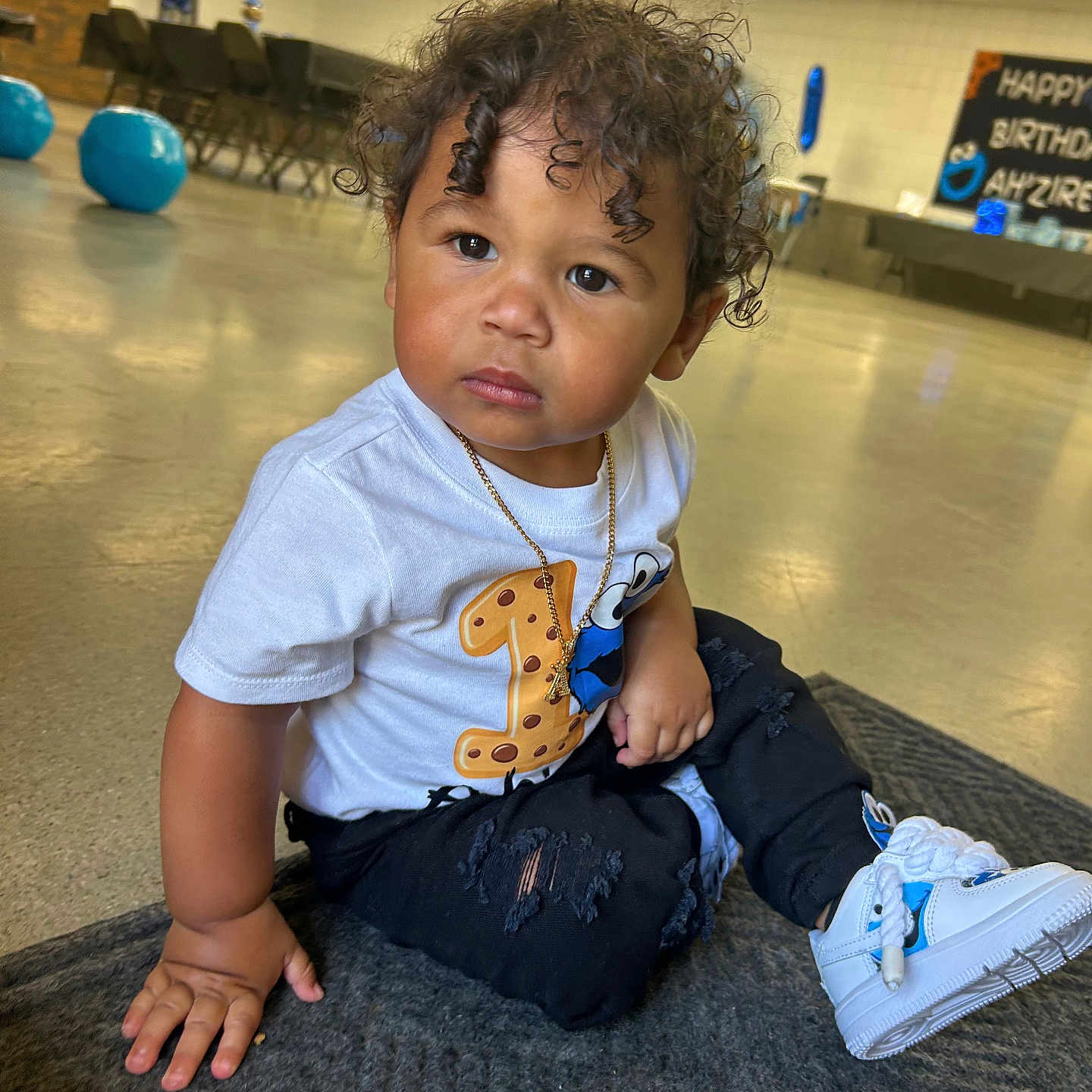 Ahzire joined the competition — help win amazing prizes! balloons, birthday_party, black_pants, celebration, child, cookie_monster, curious, curly_hair, floor, indoor, mat, necklace, number_one, party, person, ripped_pants, serious_expression, toddler, white_sneakers, white_tshirt
