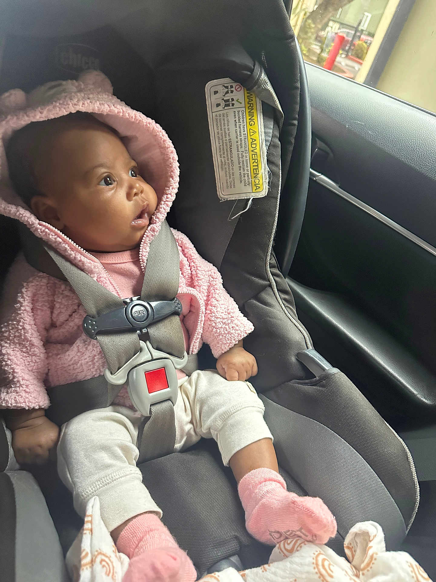 Carter is registered to the contest to win money with this photo: baby, car_seat, pink_hoodie, safety_harness, child, infant, car_interior, window, curious, seatbelt, clothing, person, sitting, sock, blanket, indoors, seat, headwear, fuzzy, young_child