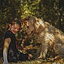 animal, autumn, black_clothing, brown, child, curly_hair, dog, forest, friendship, girl, grass, happy, leaves, nature, outdoor, pet, playful, seasonal, smile, sunlight